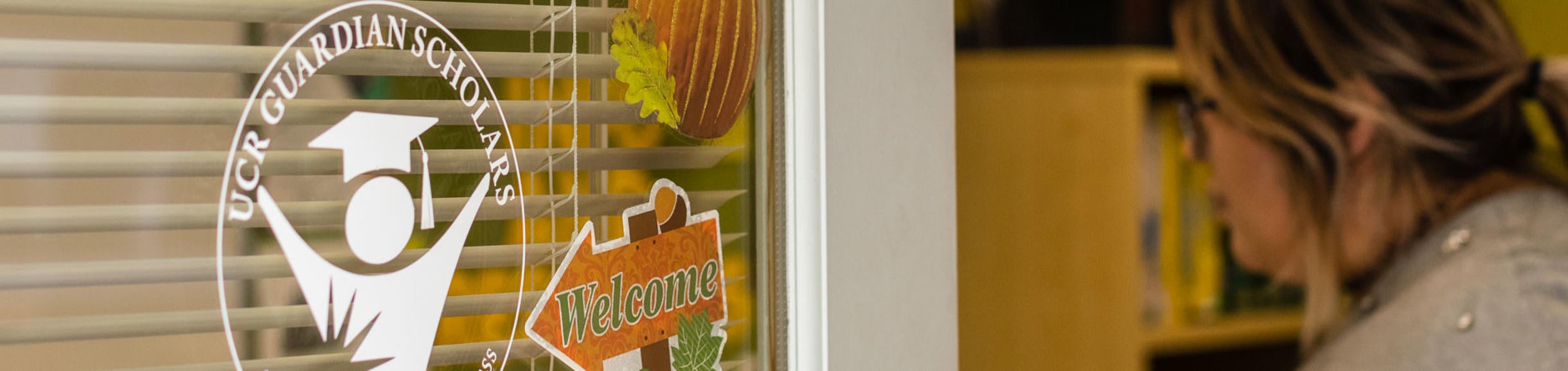 A former foster youth enters a door displaying a UCR Guardian Scholars sign